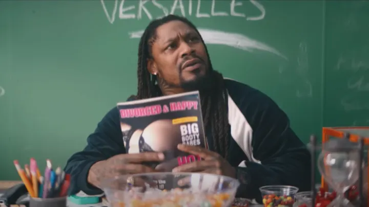 Marshawn Lynch sits in front of his blackboard, reading a porn mag entitled "DIVORCED & HAPPY."